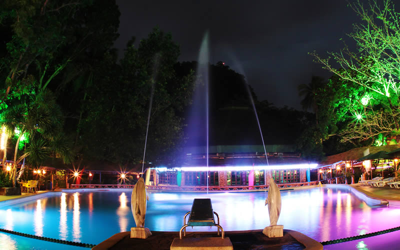 The pool at night, fountains lit in magenta and cyan.